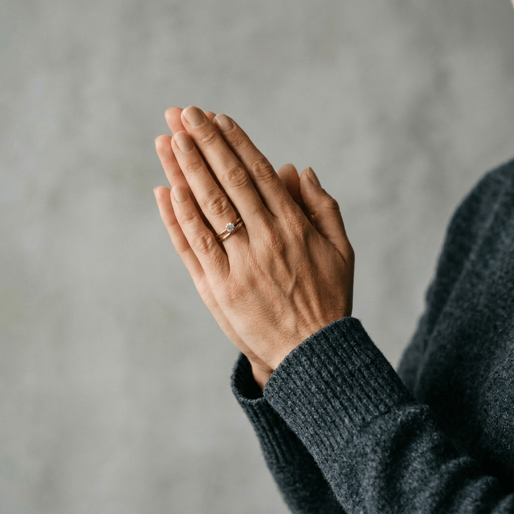 Two hands pressed together in prayer position, wedding ring visible on finger